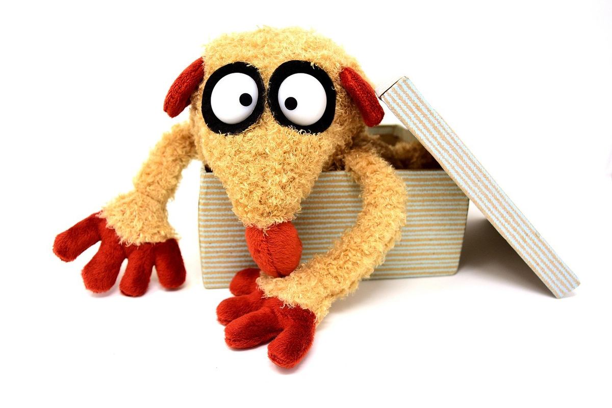 Peluche anthropomorphe aux yeux exagérés sortant d'une boîte en carton Peluche anthropomorphe aux yeux exagérés sortant d'une boîte en carton